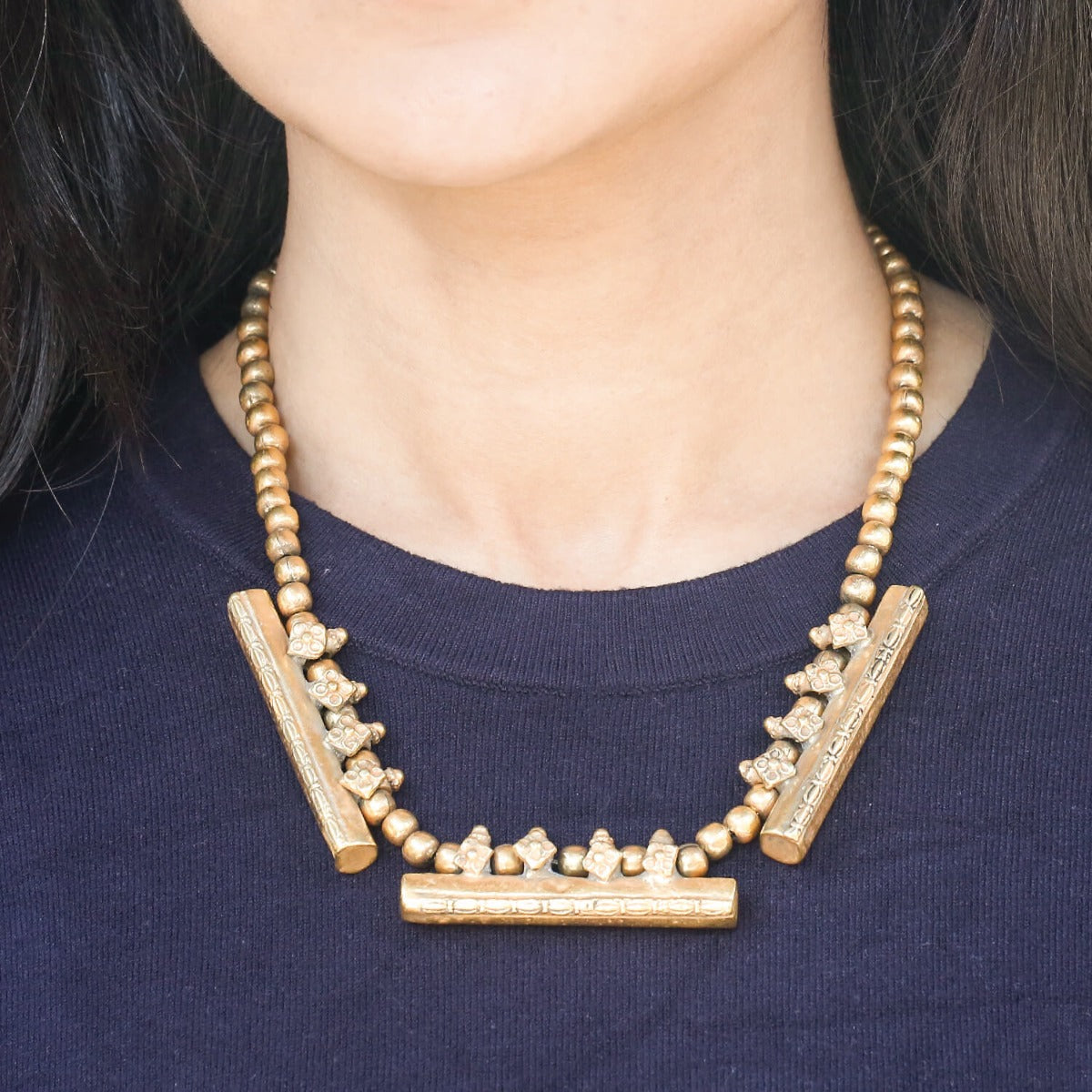 Gold necklace with bar and bead design worn by a person on a dark blue background
