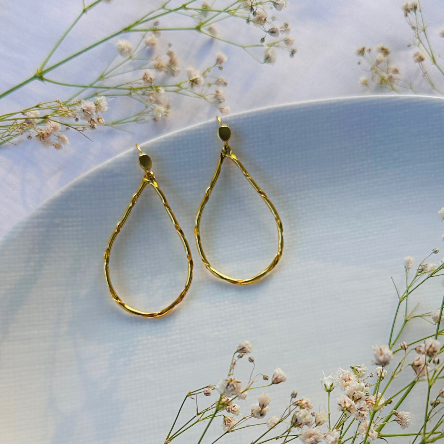 Gold plated sterling silver earrings, 18k gold plated 925 sterling silver earrings for women, Earrings, Golden earrings, Gold teardrop earrings on a light blue surface with small white flowers.