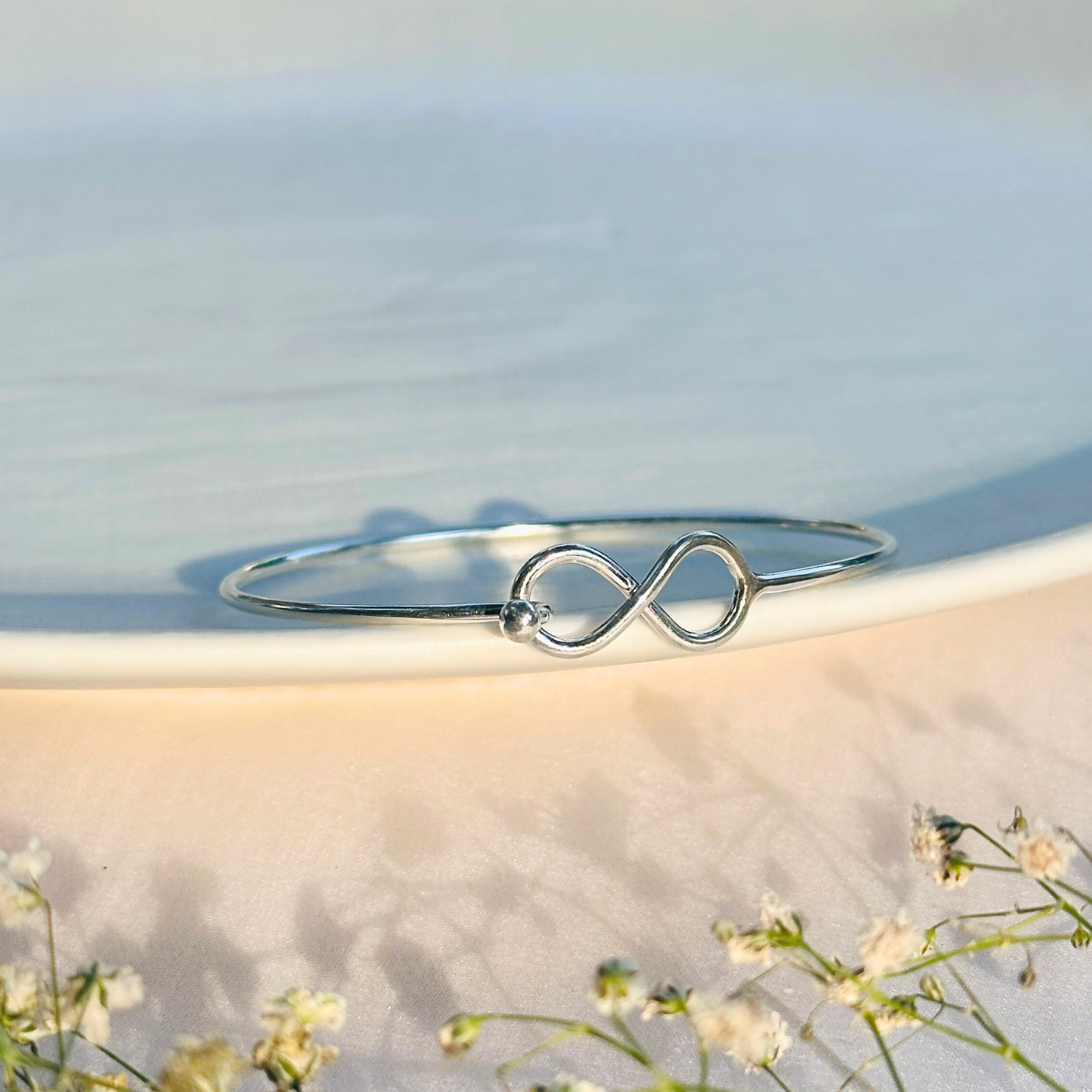 Silver infinity bracelet on a light background with flowers