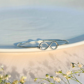 Silver infinity bracelet on a light background with flowers